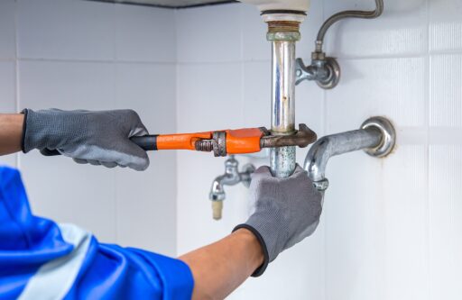 Technician plumber using a wrench to repair a water pipe under the sink | hoa responsible for water damage