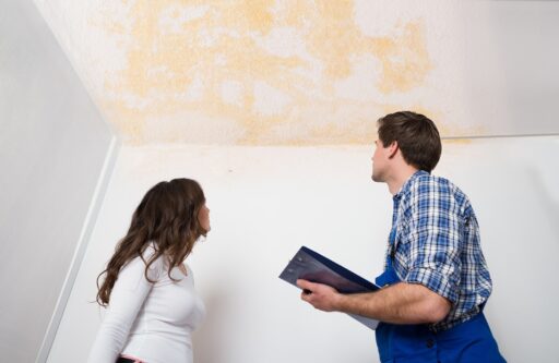 Young Worker Writing On Clipboard With Woman Standing In House | HOA responsible for water damage